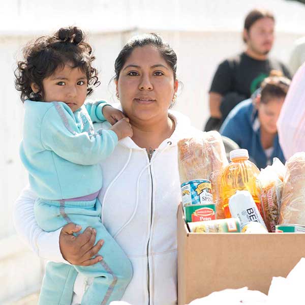 Mother holding toddler girl and a box of food