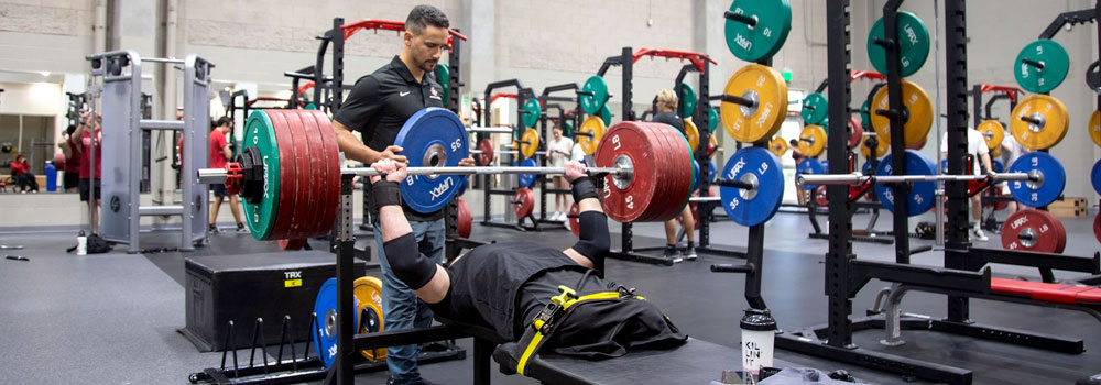Student Athlete doing a chest press with trainer next to him