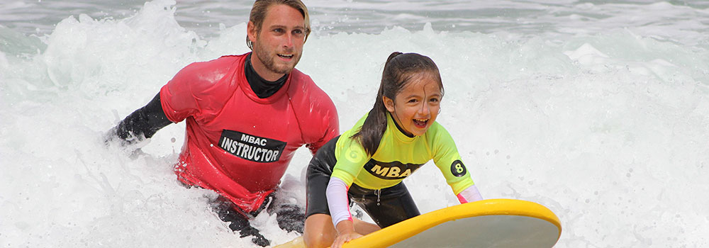 Instructor helping a girl catcha wave on surfboard at the The Watersports Camp
