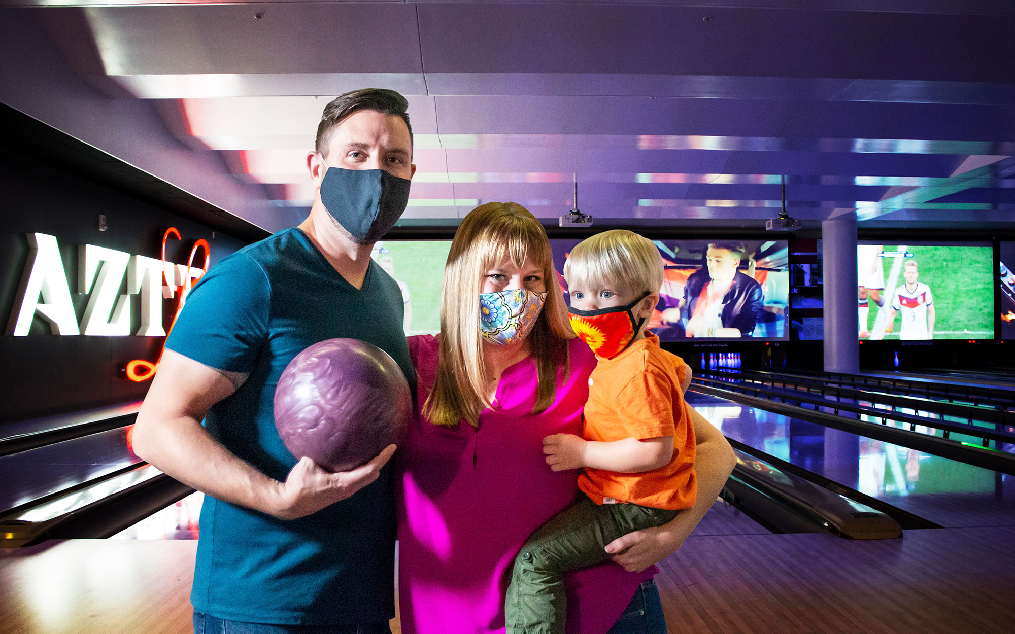 Mod, dad and kid bowling while wearing face masks