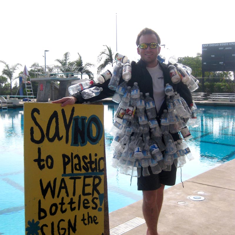 Man wearing water bottles holding a a sign agaist plastic water bottles