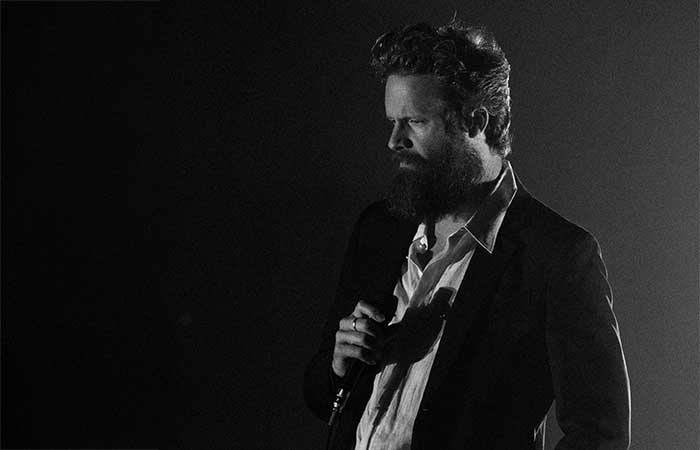 Father John Misty on stage holding a microphone Photo