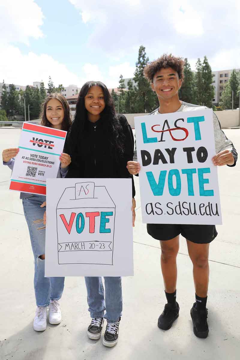 Three smiling SDSU students with Voting posters