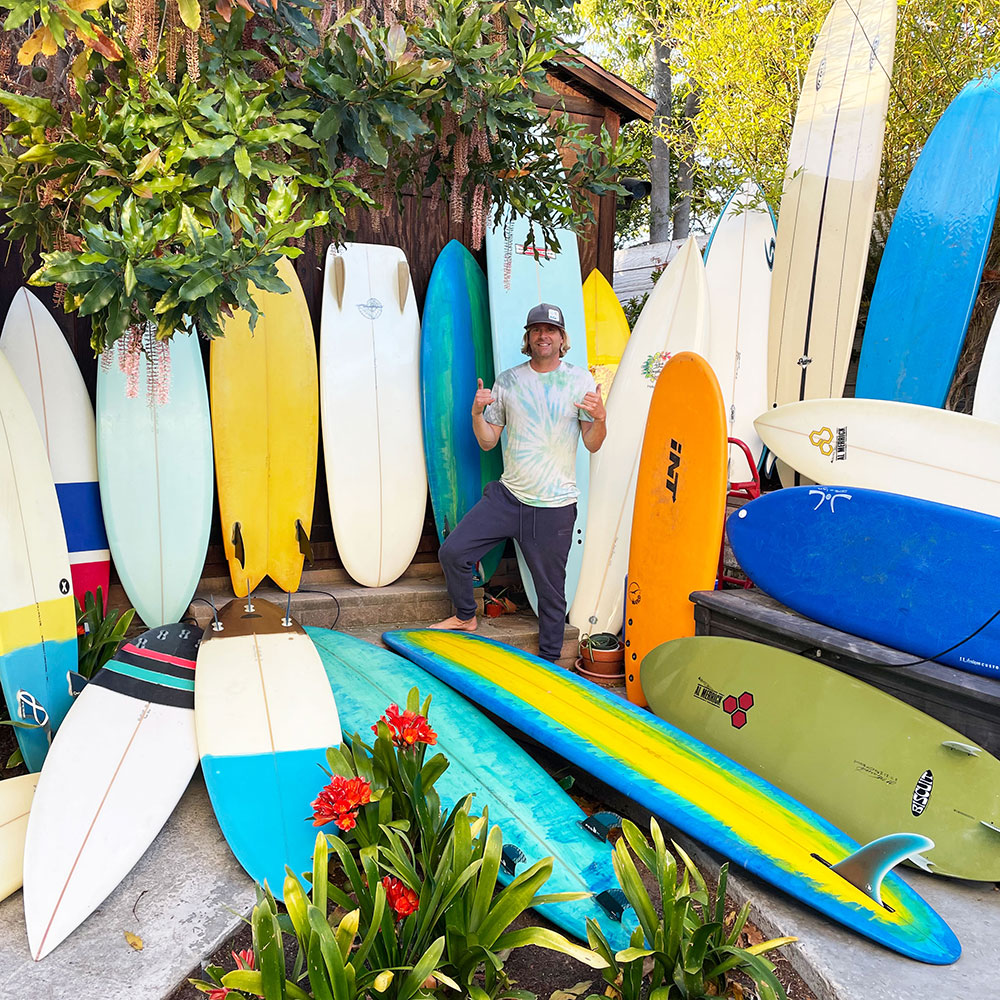 Kevin Straw standing with his collection of surfboards.