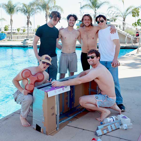 A group of SDSU students at Aquaplex with a cardboard box boat, at boat building fundraising event