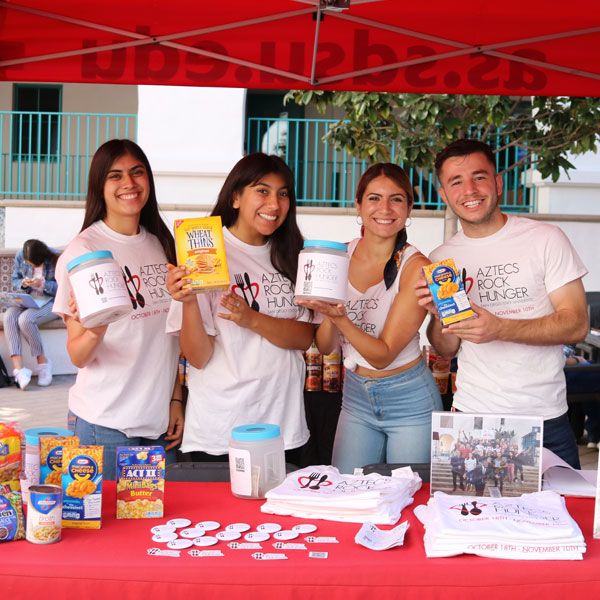 Four smiling ARH members at a tabling event showing non-perishable food and donation jars